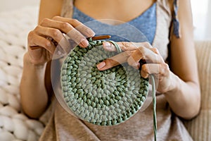 Closeup female hands knitting interior decor basket use green ribbon yarn and crochet needle