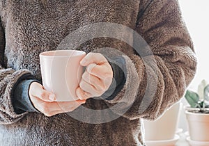 Closeup of female hands with a pink mug coffee beverage. Beautiful girl in grey sweater holding cup of tea or coffee