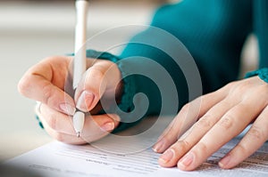 Closeup of female hands signing document in blue sweater with black pen