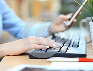 Closeup female hands typing on keyboard using smart phone at the desk in the office.