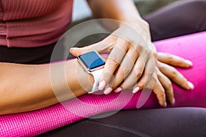 Closeup female holding pink yoga mat and checking pulse on smartwatch after sport trainings, looking at wristwatch