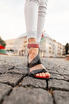Closeup of female legs with fashion summer red-black shoes and white jeans walks along a stone road in the city