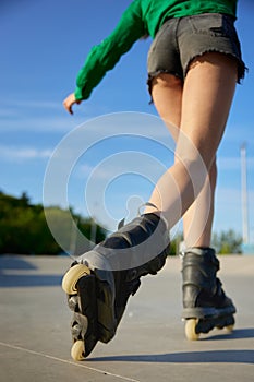 Closeup female legs wearing roller skates over asphalt rollerdrom background