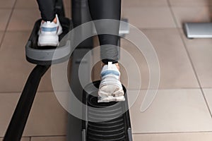 Closeup of female legs in white sport sneakers on a modern stepper simulator in a gym. Girl does exercise sports class.