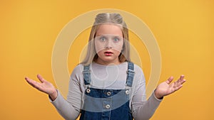 Closeup female little kid dont know puzzlement gesture with raising hands posing isolated on orange