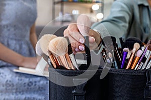 Closeup female makeup artist hands taking brush for applying cosmetics explaining to client