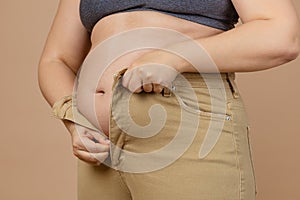 Closeup of female not able to put jeans on because of flabby large abdomen on beige background. Visceral fat. Body