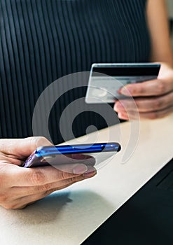 Closeup of a female's hands holding a credit card and making online transactions using mobile phone