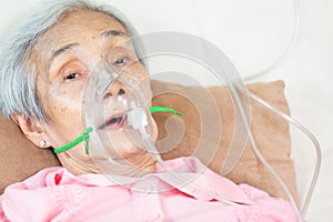 Closeup of female senior patient putting inhalation or oxygen mask in hospital bed or home,sick elderly asian woman undergoing photo