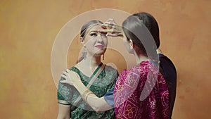 Closeup female sticking red bindi point to friend