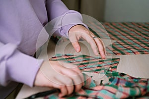 Closeup of female tailor cuting out checkered fabric with a paper pattern to make out a shirt