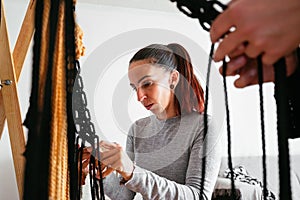 Closeup of female weaving threads and creating a macrame wall hanging decoration