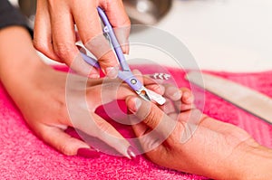 Closeup females hands getting manicure treatment from woman using nail scissors in salon environment, pink towel surface