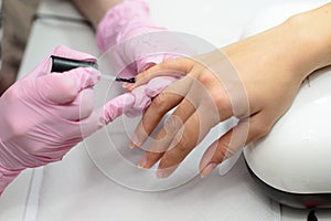 Closeup females hands getting manicure treatment from woman using small brush in salon environment, pink towel surface, blurry