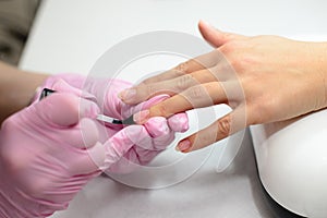 Closeup females hands getting manicure treatment from woman using small brush in salon environment, pink towel surface, blurry