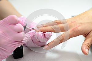 Closeup females hands getting manicure treatment from woman using small brush in salon environment, pink towel surface, blurry