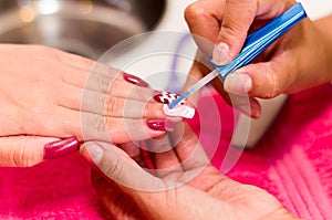 Closeup females hands getting manicure treatment from woman using small brush in salon environment, pink towel surface