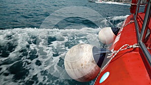 Closeup of fenders, ropes and buoys hanging on the side of red boat sailing in sea bay