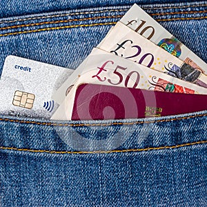 Closeup of fifty, twenty, ten pounds sterling banknotes, contactless credit card and EU passport peeking out of blue jeans back