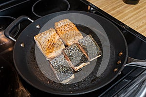Closeup of fish slices frying on the clack pan in the kitchen