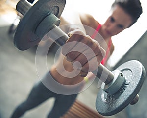 Closeup on fitness woman lifting dumbbell in loft gym