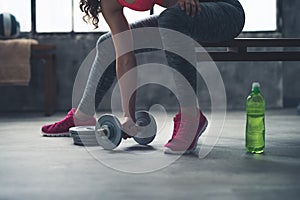 Closeup on fitness woman taking dumbbell from the floor in gym