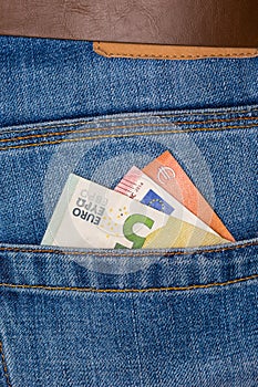 Closeup of five Euro banknote peeking out of blue jeans back pocket
