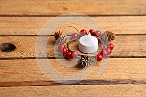 Closeup of a flameless candle and a wooden Christmas ornament with small pine cones on a table