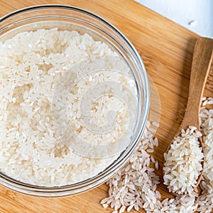 Closeup flat top lay view down of soaked rice, grain, cloudy liquid water in glass bowl on wooden background