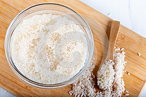 Closeup flat top lay view down of soaked rice, grain, cloudy liquid water in glass bowl on wooden background