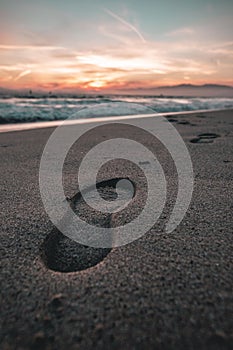 Closeup of a footstep on a sandy beach, against the vivid sunset sky