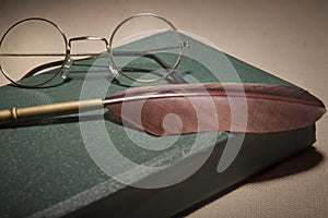 Closeup of fountain feather pen with vintage glasses on old green book. Selective focus