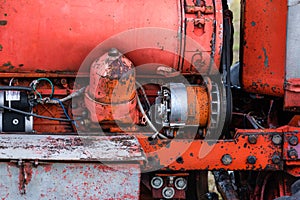 Closeup of four cylinder diesel tractor engine with visible belt rusty tracks hydraulic parts and wiring red paint in