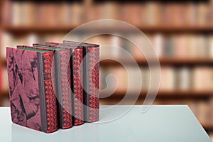 Closeup of four old books on bright table with a blurred bookshelf in library. Education concep