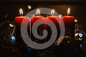 Closeup of four red candles burning with the number 2028 on them next to Christmas decorations