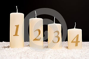 Closeup of four white Advent candles with the numbers 1 to 4 on a white surface with dark background