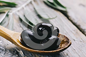 Closeup of fresh black olive in oil on rustic wood table. Organic olive fruit in kitchen wooden spoon