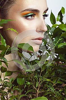 Closeup fresh face of an attractive caucasian girl with green plants. Model with bright brown eye makeup.