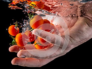 Closeup of fresh and health cherry tomatoes falling into clear water with big splash on black background. Group of fresh tomatoes