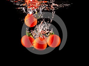 Closeup of fresh and health cherry tomatoes falling into clear water with big splash on black background. Group of fresh tomatoes