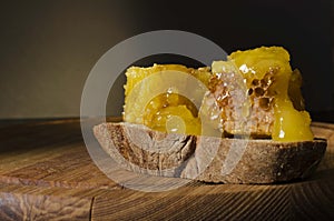 Closeup of fresh honeycomb,piece of rye bread on the wooden boardagainst dark background