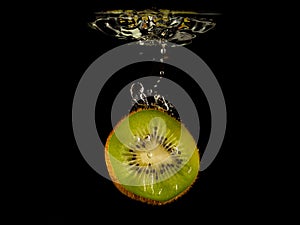 Closeup of fresh kiwis slices falling into clear water with big splash on black background. Group of juicy kiwi falling into water