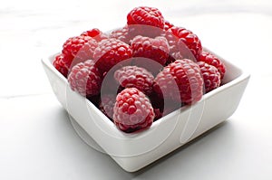 Closeup of fresh and ripe raspberries in the white bowl, white table