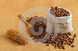 Closeup of freshly roasted coffee beans on a wooden table with a sack, spoons and cinnamon rolls
