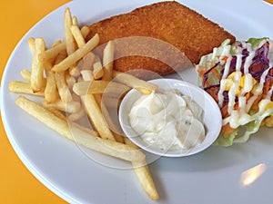 Closeup fried fish, chips and salad on a white dish on yellow ta