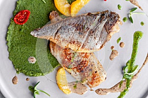 Closeup fried sea bass fillet with green pea puree, tomatoes, sauce, orange slices. Concept professional photography, photosession
