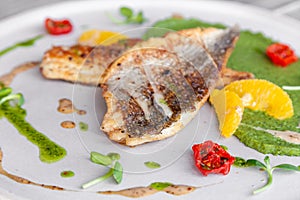 Closeup fried sea bass fillet with green pea puree, tomatoes, sauce, orange slices. Concept professional photography, photosession