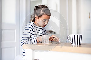 Closeup front view of a elementary school girl eating a burger at a home. She`s looking at camera and making funny faces