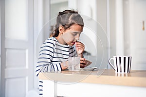 Closeup front view of a elementary school girl eating a burger at a home. She`s looking at camera and making funny faces