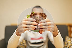 Closeup funny blurred protrait of young man hold bitten sandwich by his two hands. Sandwich in focus. light background